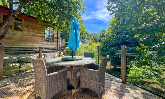 External of a lodge on pitch with decking and table and chairs among woodland