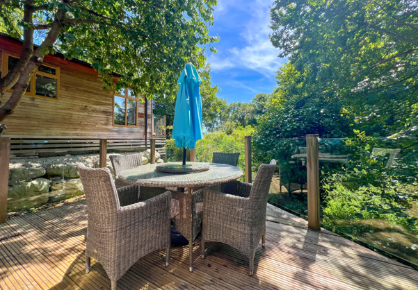 External of a lodge on pitch with decking and table and chairs among woodland