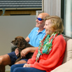 A couple sat on outdoor furniture on the decking of a lodge with a dog