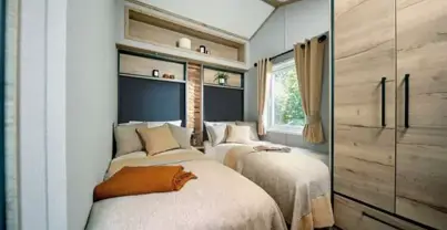 Twin room with cosy bedding, compact self-contained wardrobe, and shelving above the bed