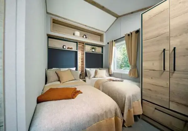Twin room with cosy bedding, compact self-contained wardrobe, and shelving above the bed
